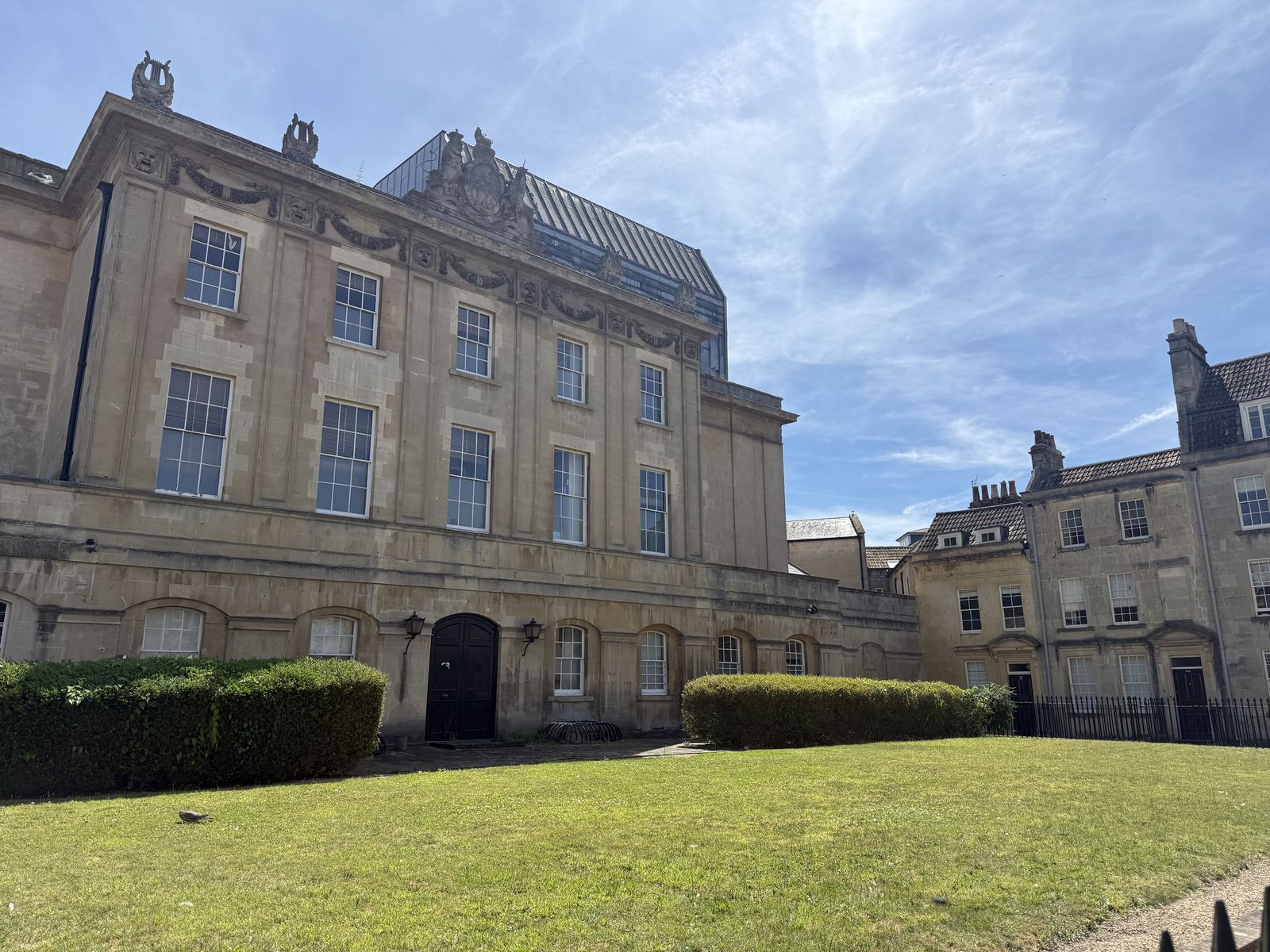 A grand Georgian facade in golden Bath stone behind a neat green lawn